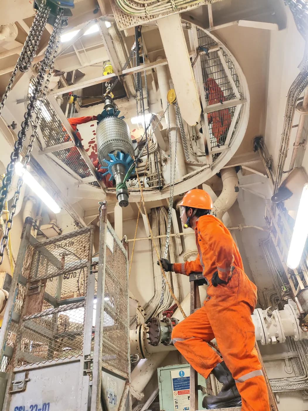 Technician in orange coveralls climbing a ladder in a ship's engine room